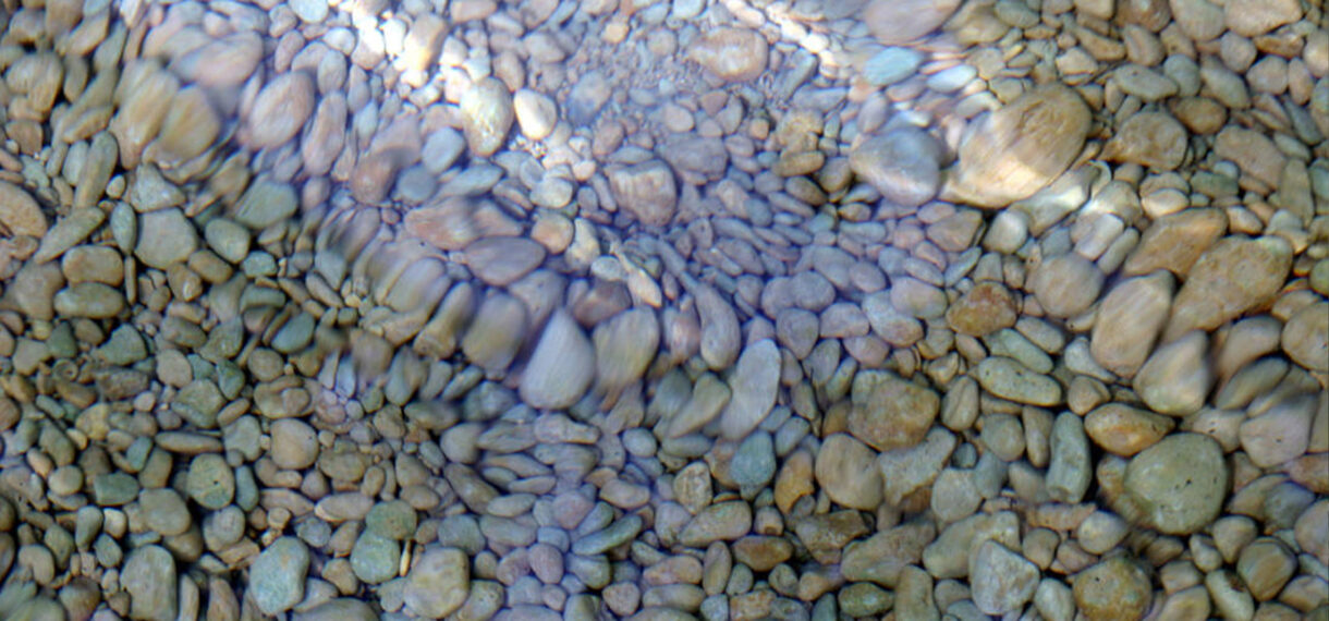 Rocks at the bottom of the river shine as the water flows over them.